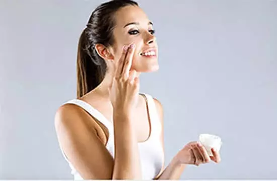 a young lady applying face shimmer lotion to her face
